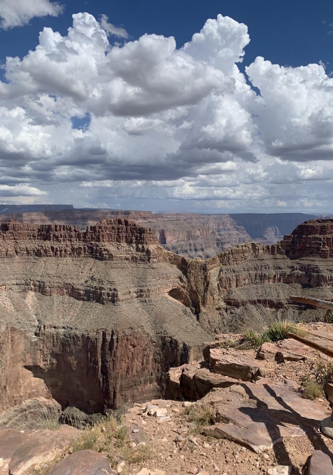 Blick vom Rand des Grand Canyon über rote, zerklüftete Felsschichten, darüber ein weiter Himmel mit hohen Wolken